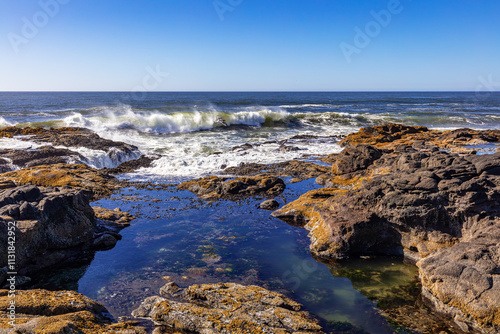 Tide pool and crashing waves on the central Oregon coast with blue sky, USA. 