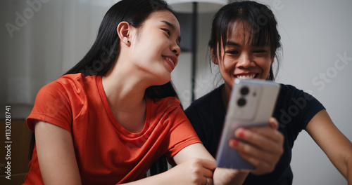 Portrait of Two siblings happily chatting on the floor and using mobile phone to check if the items in the boxes they moved from old house are complete. Moving to a new home concept photo