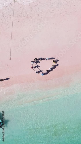 Aerial top drone view of people holding hands and enjoying holiday at Pink Beach Island in Labuan Bajo.