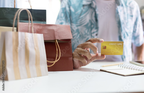 Asian man in sitting at home with shopping bags on table and holding credit card to checking transaction from online shopping before pay photo