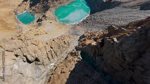 Predaccio, Valmalenco, Lombardy, Italy - A Turquoise Lake Glistens Amid Rugged, Rocky Terrain With Snow-capped Peaks Under a Clear Blue Sky - FPV Shot photo