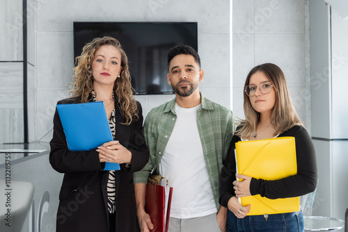 Confident business team holding documents, standing together in modern office meeting room, demonstrating teamwork and professionalism