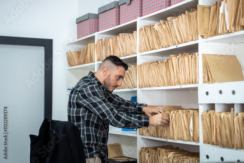 Office worker searching through files in an archive room filled with shelves of documents, ensuring efficient organization and retrieval of information