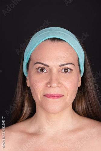 Portrait of a smiling 40-year-old woman with light blue headband, calm expression and natural face on black background. Concept of woman, maturity and natural beauty