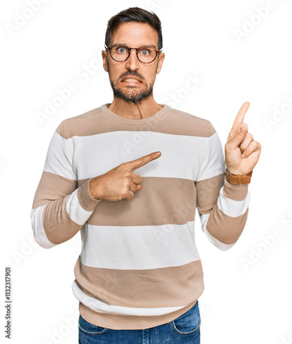 Handsome man with beard wearing casual clothes and glasses pointing aside worried and nervous with both hands, concerned and surprised expression