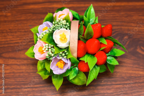 Delicate bouquet of soap in the form of flowers and strawberries in a wooden basket brown background. Handmade exclusive work.