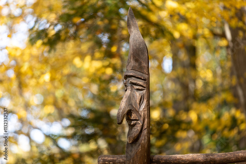 Fototapeta Naklejka Na Ścianę i Meble -  a head carved in wood by an unknown artist against the background of a forest in autumn colors