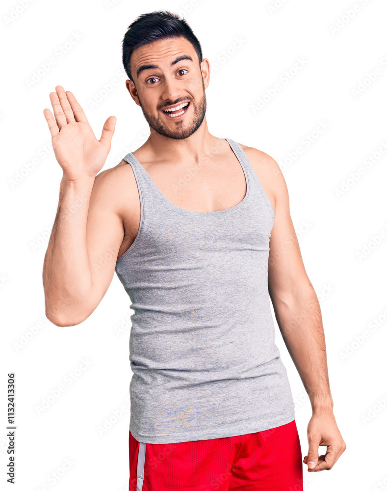 Fototapeta premium Young handsome man wearing swimwear and sleeveless t-shirt waiving saying hello happy and smiling, friendly welcome gesture
