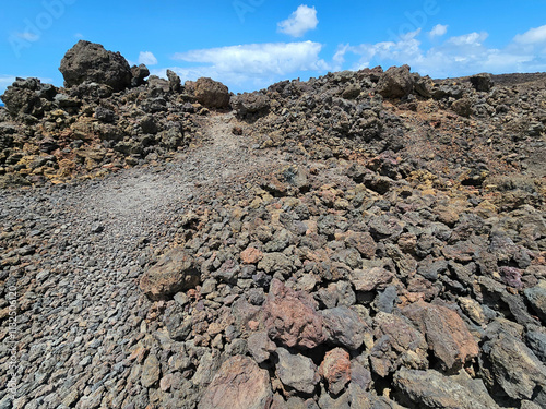 Un paysage volcanique brut à Lanzarote dévoile une accumulation de roches volcaniques aux teintes variées, sous un ciel bleu parsemé de nuages. photo