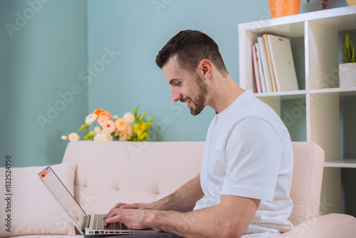 Smiling man using a laptop while sitting on a sofa in a cozy living room