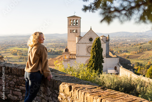 Young woman enjoying the view of Basilica of St. Francis in Assisi hilltop town of Umbria, Italy.