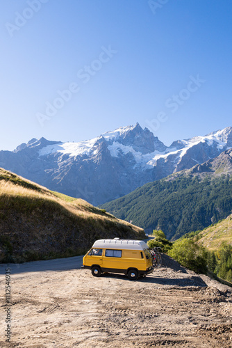 Yellow retro camper van exploring the Alps with high mountains in the background, Ecrins national park, France