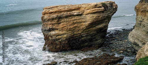 Seascape featuring a unique rocky formation along the coastline surrounded by gentle waves and pebbly shoreline elements.