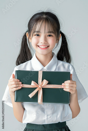 A teen girl in a school uniform, hugs a present box with both arms while smiling brightly. radiates happiness, standing in front of a plain background,  photo