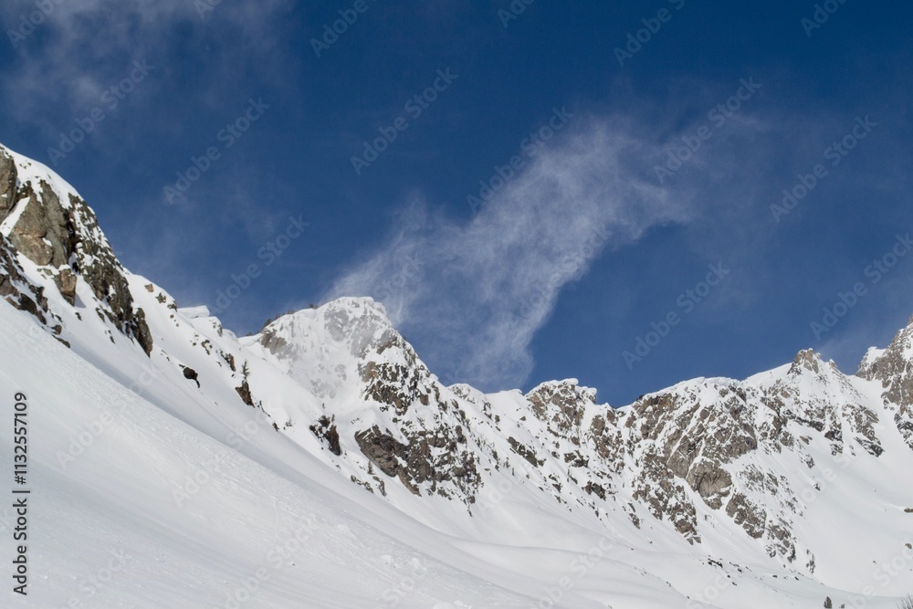 Obraz premium Snow blows off the summit of a mountain in Beehive Basin, a winter scene with blue sky in Montana