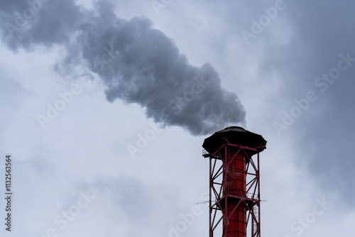 Red and white pipe with metal stocks and thick smoke against the background of a cloudy sky.