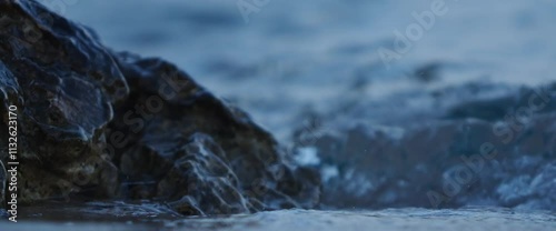 4K Slow motion ocean or sea waves crashing over rocks, water flowing naturally, crystal-clear stream, tranquil water flow, ocean waves cascading over rocks in serene natural setting of blue hour