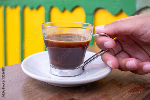 A Hand Holding A Glass Cup Of Fresh Espresso Coffee Against A Colorful Background In Colombia