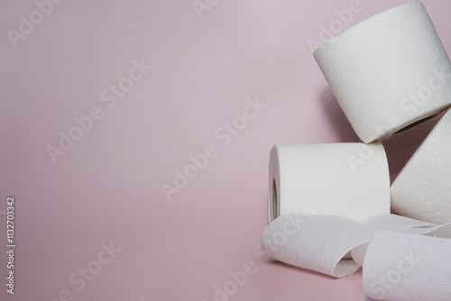 Toilet paper rolls creatively arranged on a pastel pink background. The minimalist setting highlights hygiene, cleanliness, and daily essentials