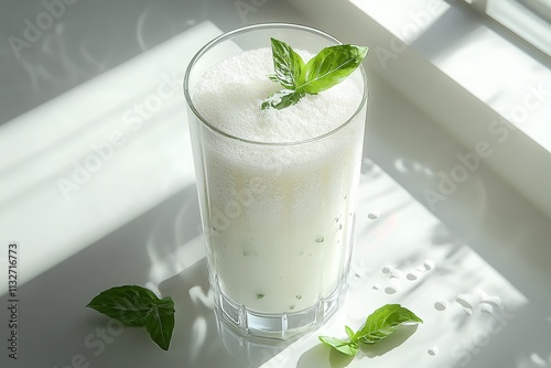 A glass of ayran drink with frothy top, garnished with a sprig of mint.