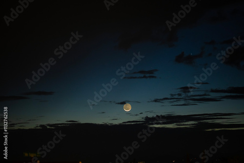 A thin crescent moon rising in the early dawn sky