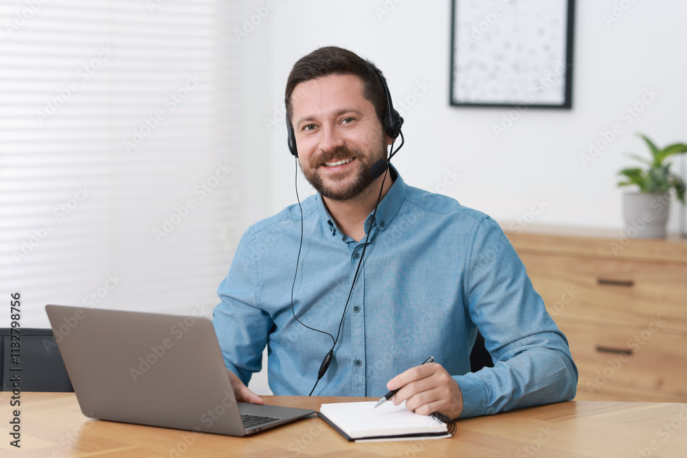 Obraz premium Interpreter in headset taking notes while having video chat via laptop at wooden table indoors