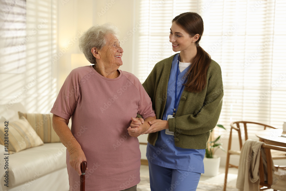 Obraz premium Caregiver assisting senior woman with walking cane indoors. Home health care service