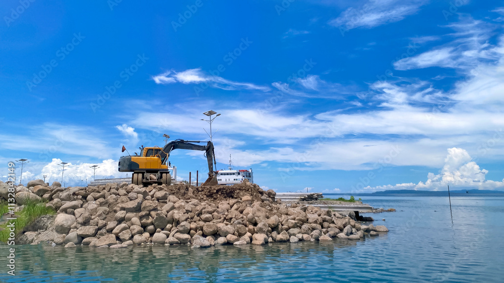 Obraz premium yellow excavator works against the background of the sky and sea in the seaport