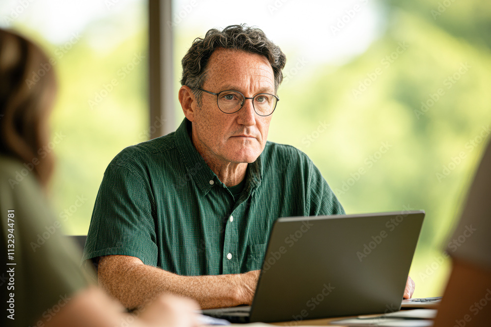 Fototapeta premium A man wearing glasses is sitting at a table with a laptop
