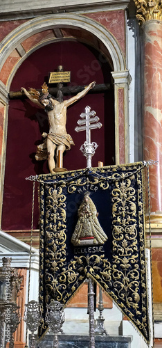 Crucifix on an altar with a banner displaying Mater Ecclesiae and embroidered religious symbols, surrounded by ornate decorations and church architecture; photo