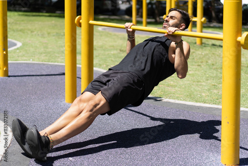 Fit young man executing inverted rows on outdoor gym bars photo