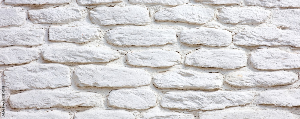 Fototapeta premium A textured, white stone wall with irregularly shaped bricks, offering a clean and minimalist aesthetic.