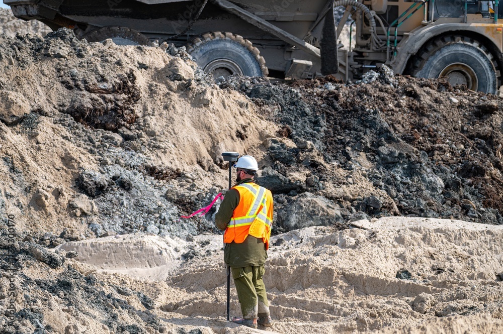 © Larry Dallaire - Surveyor carrying out a GPS survey on a construction site, with a dump truck in the background © Larry Dallaire - Surveyor carrying out a GPS survey on a construction site, with a dump truck in the background