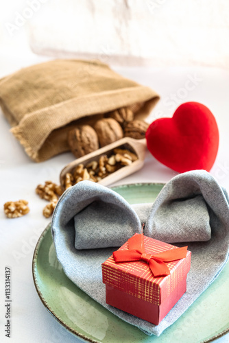 Closeup of heart shaped napkin on a plate with a gift, table decorated for romantic meal. Valentine and love concept