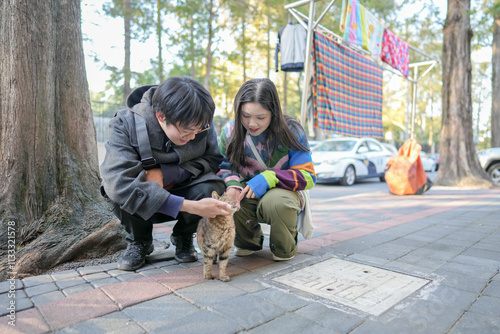 In December 2024, a young Chinese couple in their 20s pet a cat on the sidewalk in Hongkou District, Shanghai, People's Republic of China, during the cold season. photo