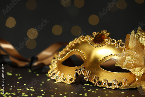 Beautiful carnival mask and confetti on dark background with blurred lights, closeup photo