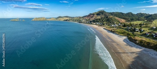 OPITO BAY, COROMANDEL PENINSULA, NEW ZEALAND, Coastal town nestled on a beautiful beach. Houses line the shore, waves crash on the sand. Aerial view. photo