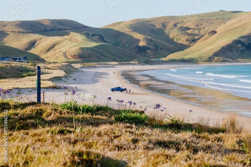 Tranquil beach scene with a blue truck parked on the sand. Hikers enjoy the coastal scenery. Coastal beauty. , OPITO BAY, COROMANDEL PENINSULA, NEW ZEALAND photo