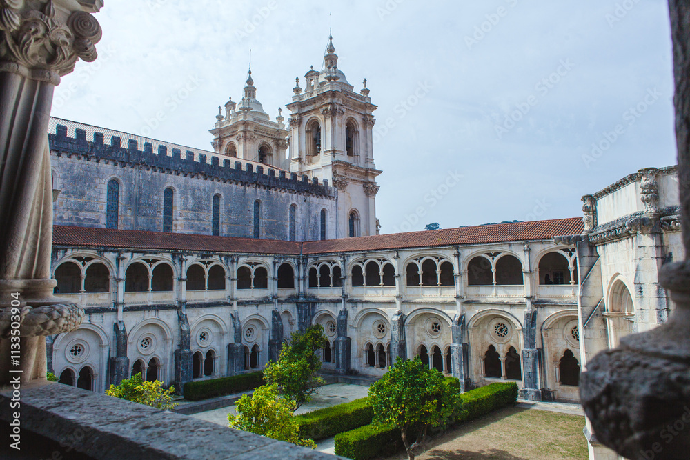 Obraz premium picturesque view through a stone archway, showcasing the architectural grandeur of a historic monastery with its ornate facade, intricate details, and a lush green courtyard
