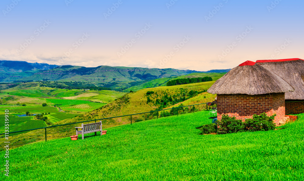 Hilltop house with a thatched roof and a bench on the edge, overlooking the Drakensberg Mountain and the valley below, KwaZulu-Natal, South Africa