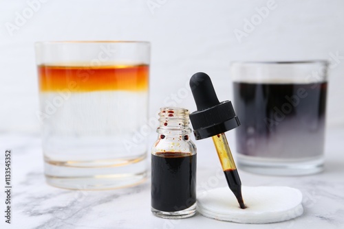 Bottle of aqueous iodine and glasses with liquids of different colors on white marble table, selective focus