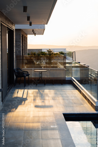 Stylish balcony with a table and chairs, illuminated by sunset light, overlooking a serene landscape and modern architecture. Luxury accommodation for unforgettable vacation. high standard of living  photo