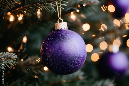 Purple Christmas ornament hangs on Christmas tree. Twinkling fairy lights create festive atmosphere. Festive decoration. Holiday season. Beautiful Christmas tree. Cozy home scene. Winter holidays. photo