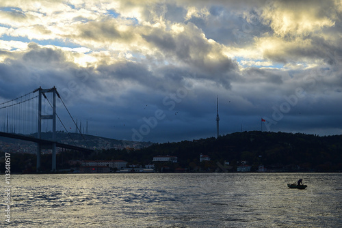 A boatman at sunrise in Ortakoy. View of the July 15 Martyrs Bridge (Bosphorus Bridge) and Camlica Mosque at sunrise.