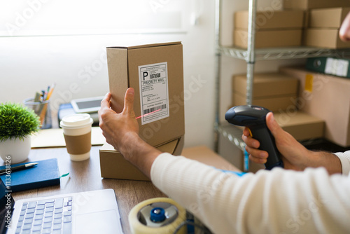 Closeup of a man preparing a shipment and scanning a barcode on a cardboard box in a warehouse using a barcode scanner photo