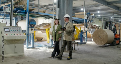 The boss scolds a paper mill worker, they walk around the workshop. A man holds a tablet in his hand