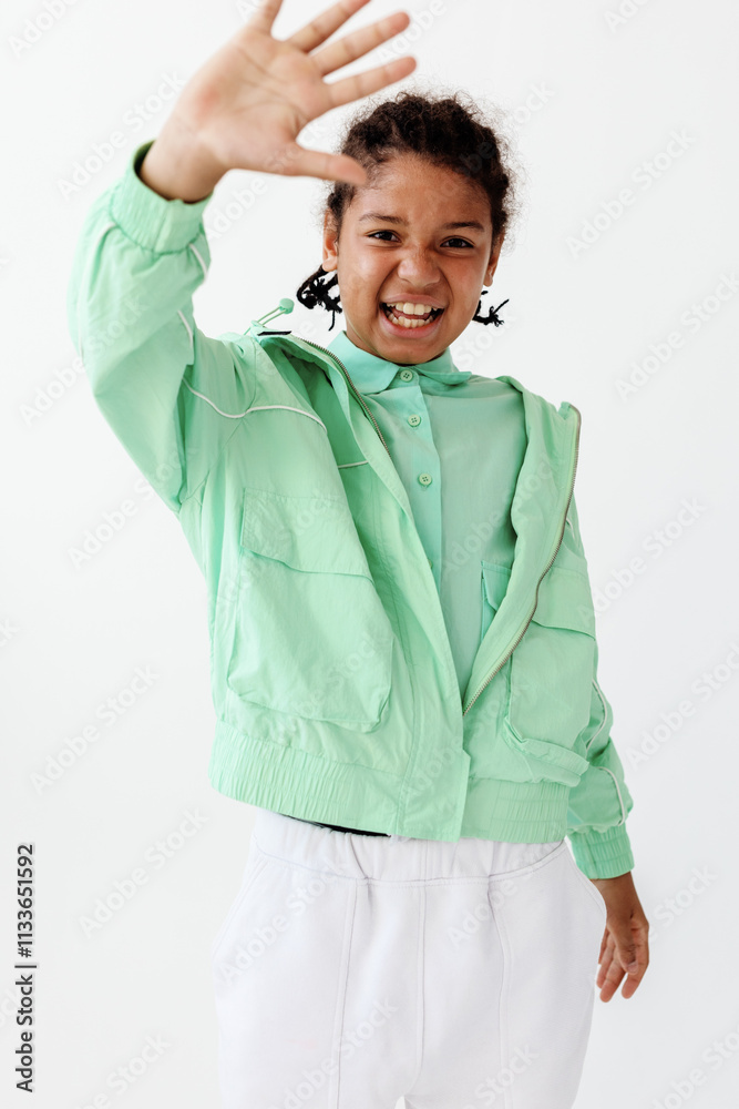 Excited young boy in stylish green jacket and white pants raising hand in air with enthusiasm Excited young boy in stylish green jacket and white pants raising hand in air with enthusiasm