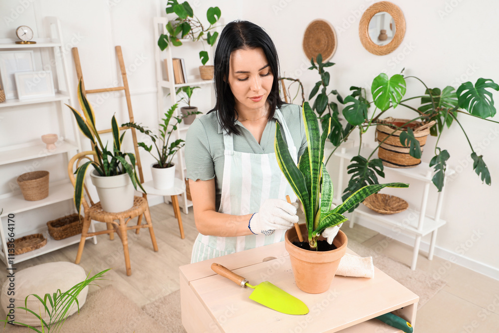 Beautiful young woman with gardening tools taking care of houseplant at home