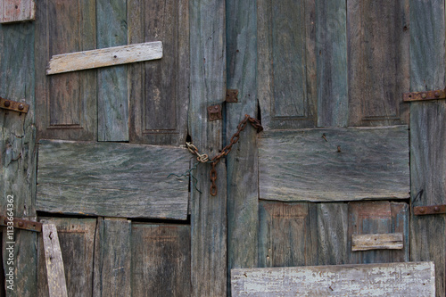 old farm door with faded blue color and worn by time with several pieces of repair wood, nails and rusty steel chain and wire functioning as a lock 1
 photo