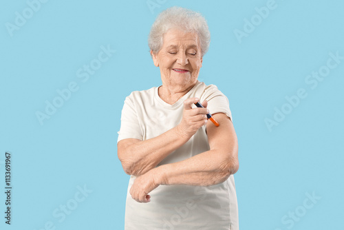 Diabetic senior woman using lancet pen on blue background photo